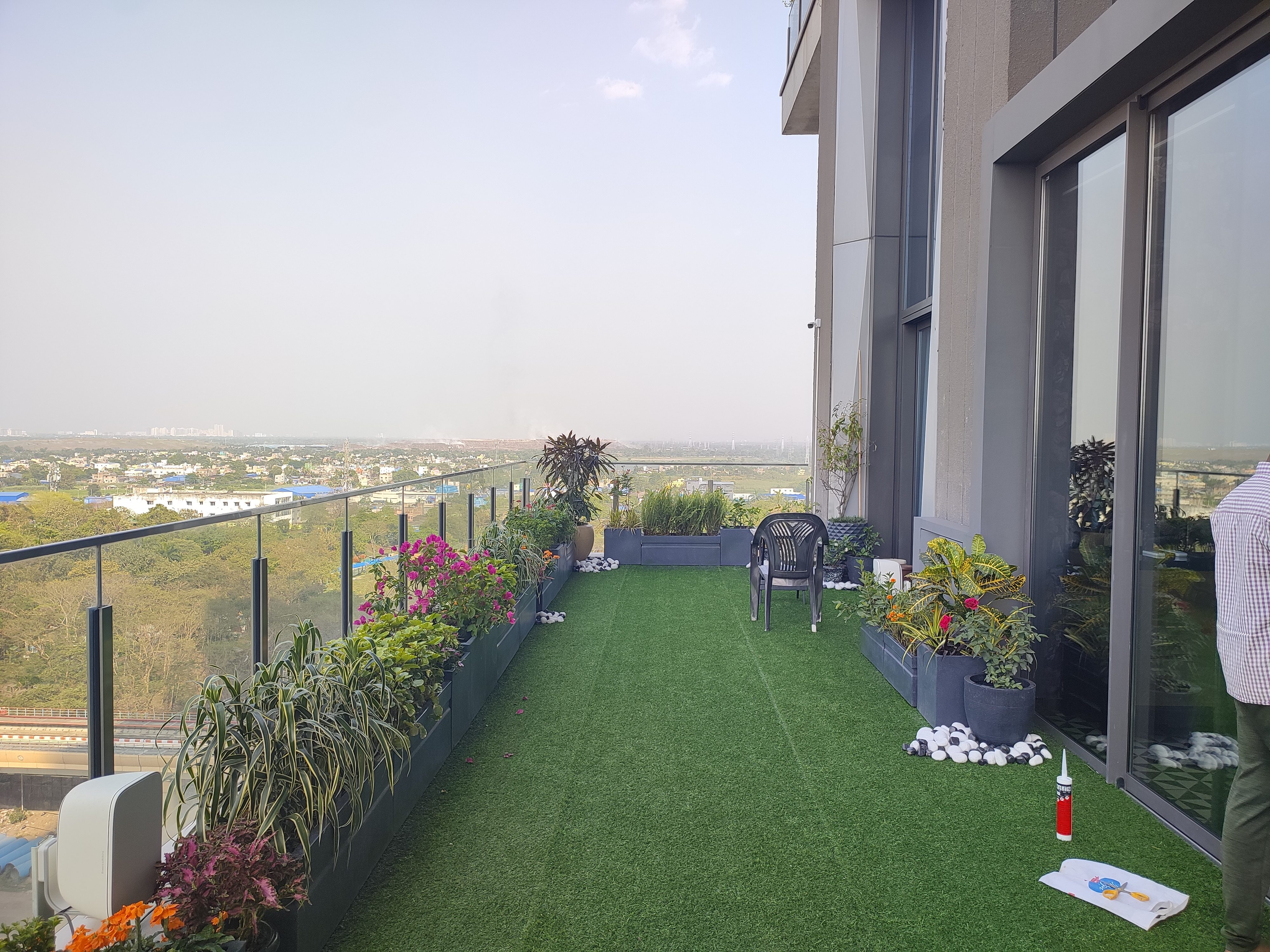 After — completed terrace with green turf, planters, and glass railing